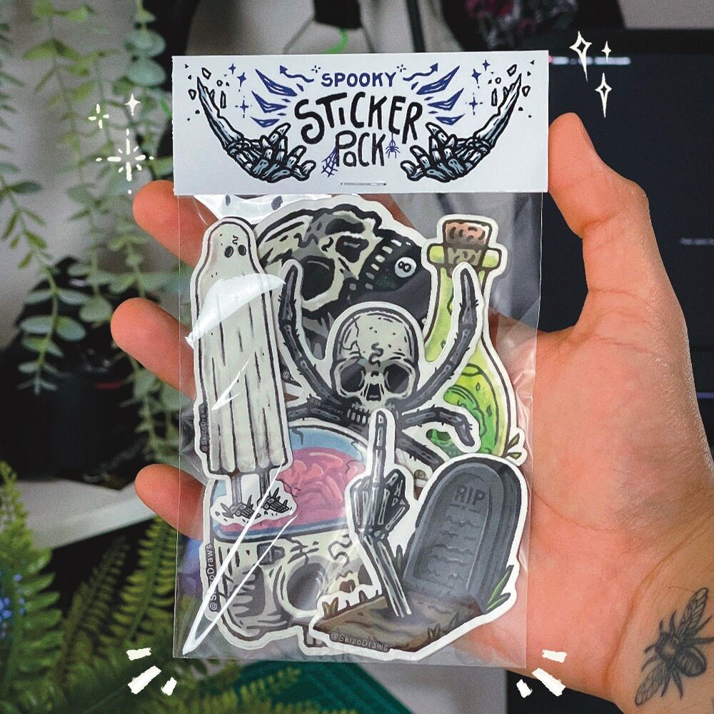 Hand hält ein Sticker-Pack mit gruseligen Cartoon-Stickern und dem Header „SPOOKY STICKER PACK“ vor einem Hintergrund aus Pflanzen