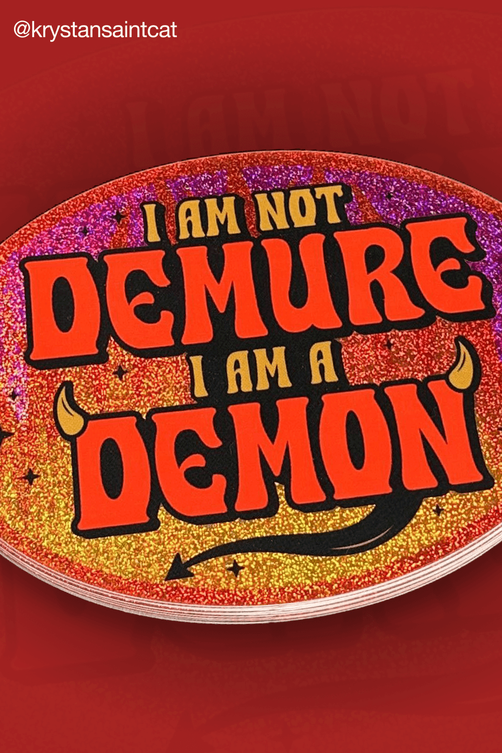Ovaler Glitzer-Aufkleber in Rot und Gold mit dem Text "I am not demure, I am a demon", Teufelshörnern und Schwanz