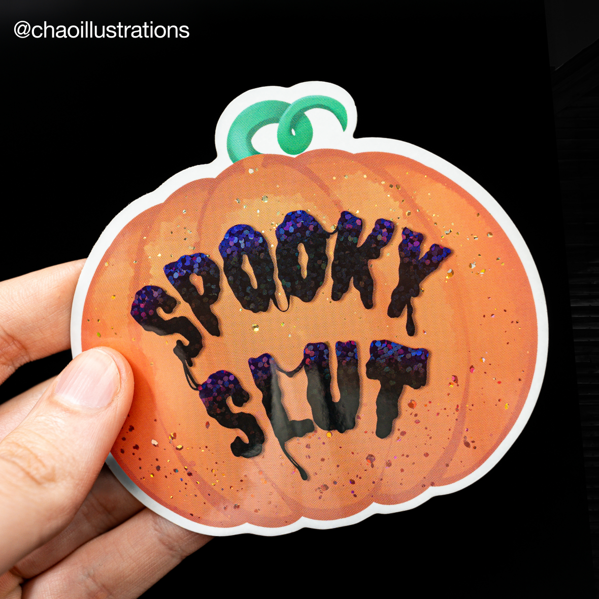 Hand hält einen konturgeschnittenen Kürbis-Aufkleber mit holografischem Glitzer-Schriftzug "Spooky slut"