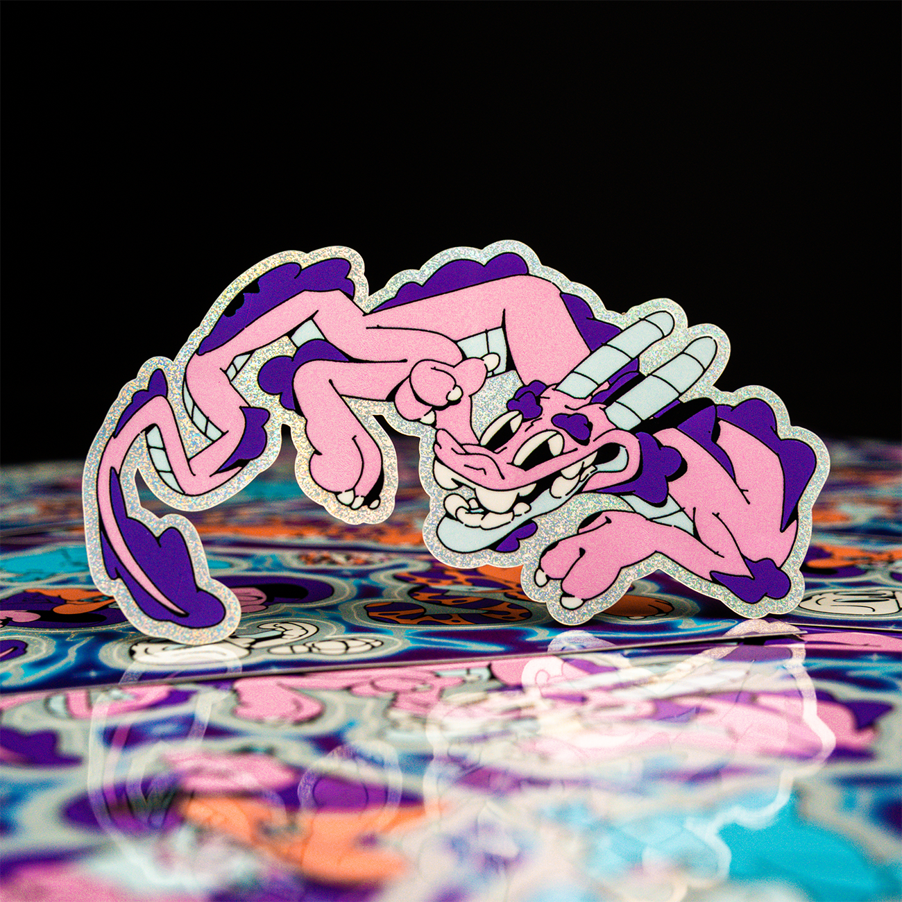 Die-cut sticker of a cartoon dragon in pink and purple, printed on Pixie Dust, with stickers in teh foreground.