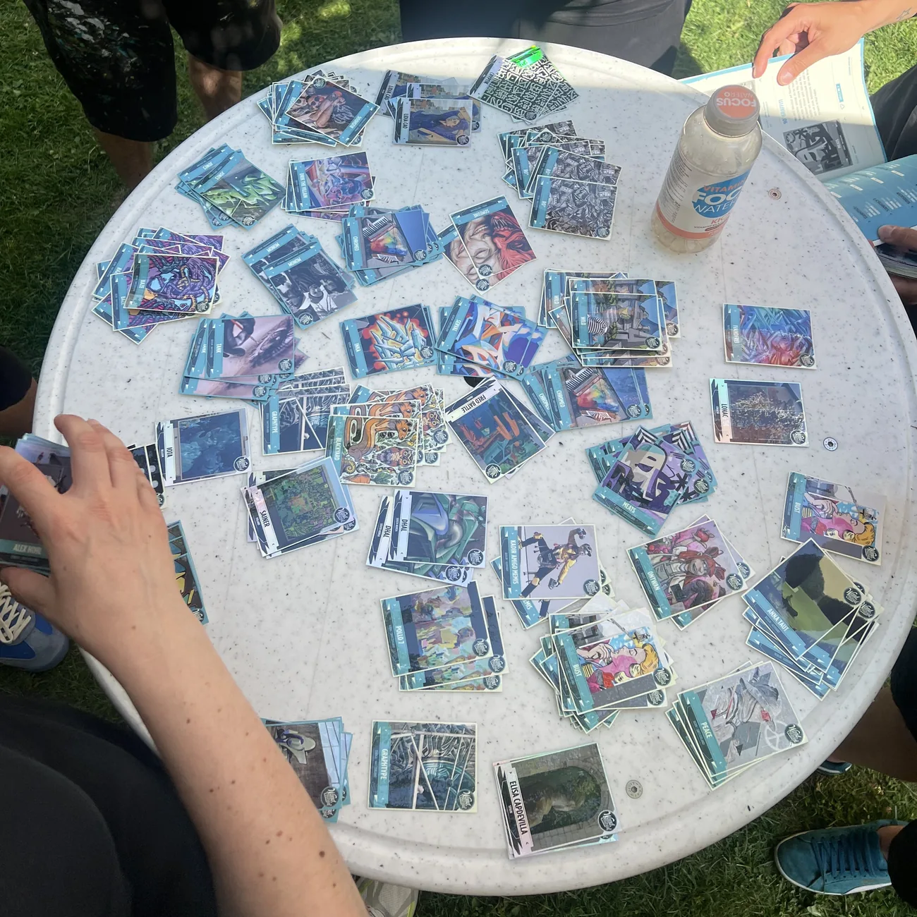 Festivalbesucher füllen blaue Stickeralben mit Street-Art-Sammelstickern, die auf einem runden Tisch verteilt liegen