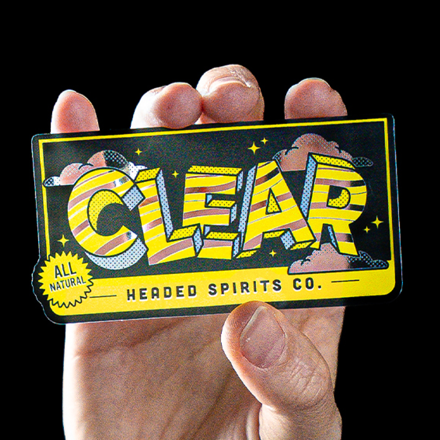 Transparenter Aufkleber mit gelb-schwarzem "Clear Headed Spirits Co."-Design in einer Hand