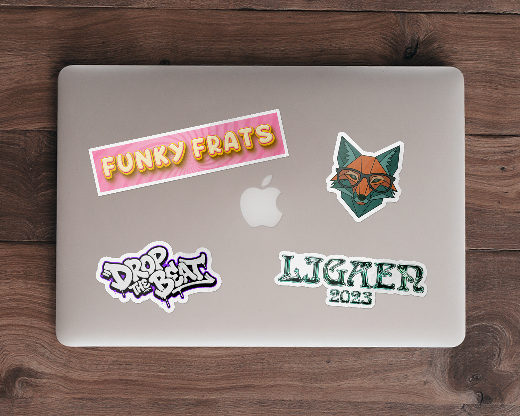 Silberner Laptop auf einem Holztisch mit vier Freiform-Laptop-Stickern, darunter ein Fuchs mit Brille