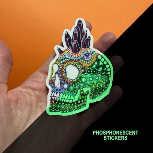 Hand hält einen Mandala-Totenkopf-Sticker von mpgautheron, zur Hälfte im Dunkeln grün leuchtend