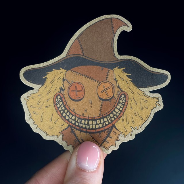 Eine Hand hält einen Kraftpapieraufkleber mit einer Vogelscheuche