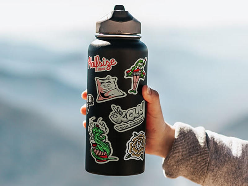 Eine Hand hält eine schwarze Wasserflasche mit sieben Stickern